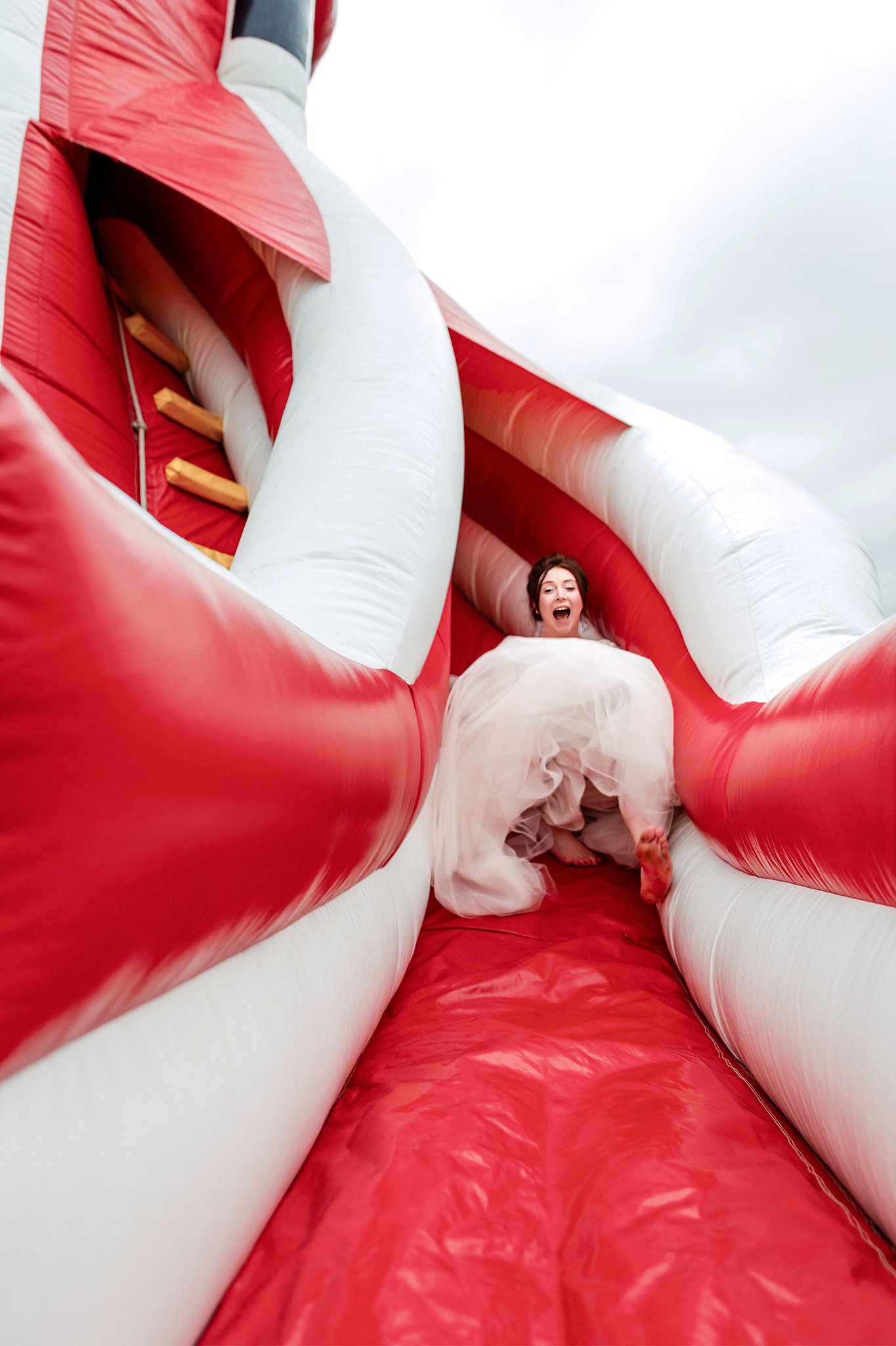 Bride sliding down an inflatable slide in her wedding dress
