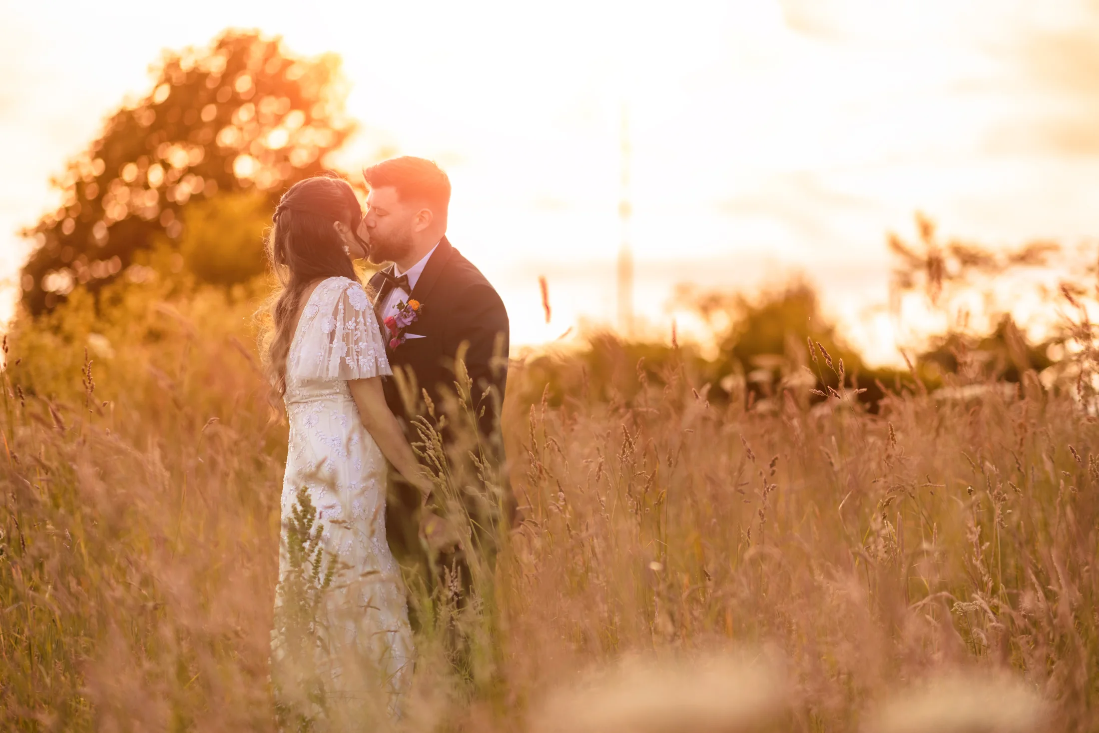 A couple kissing in tall grass in golden evening light at The Chester Fields