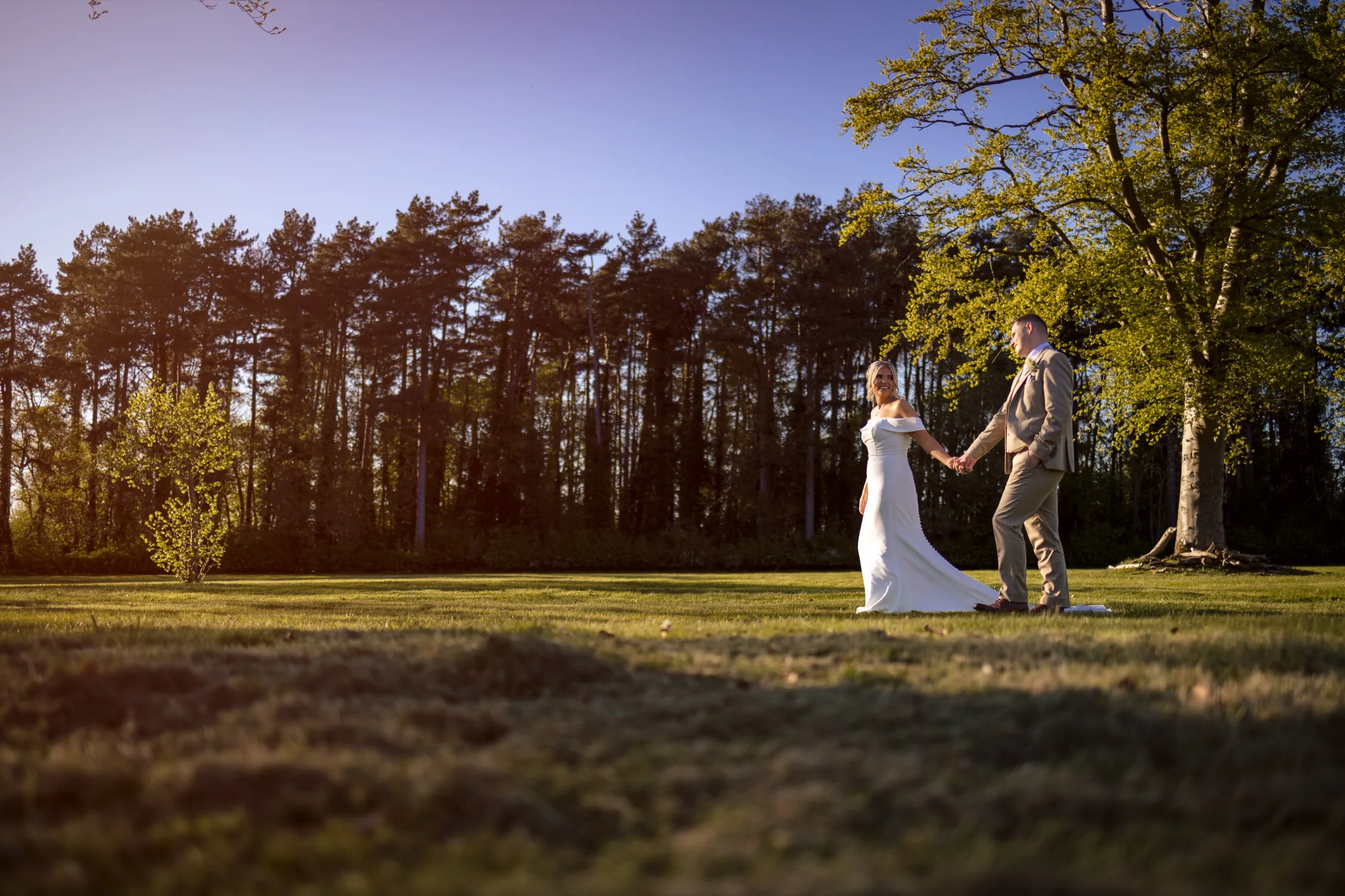 A couple walking hand in hand across the sunlit lawn at Inglewood Manor