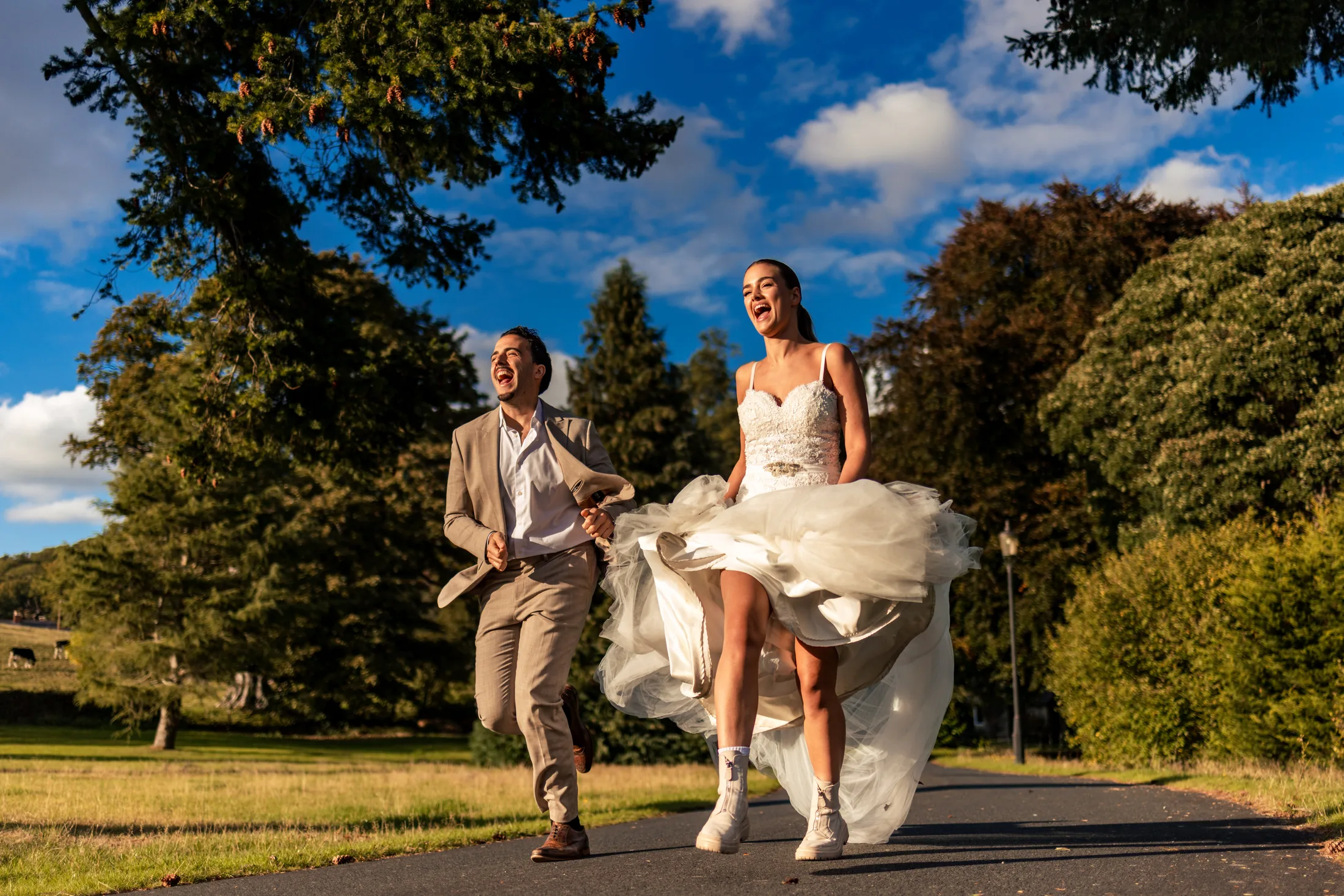 Bride and groom laughing as they run together along a tree-lined path