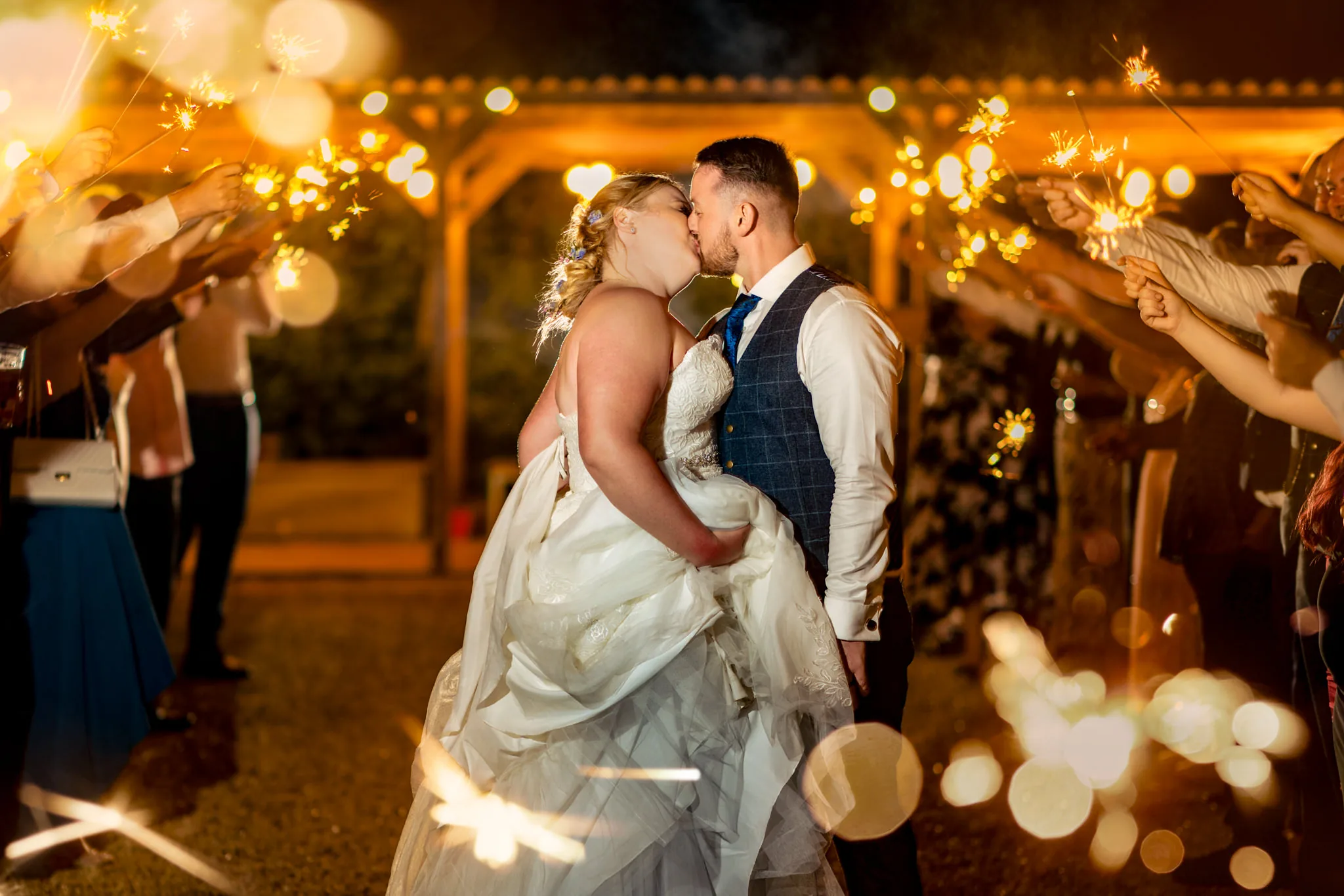 Newlyweds kissing beneath guests’ sparklers at night
