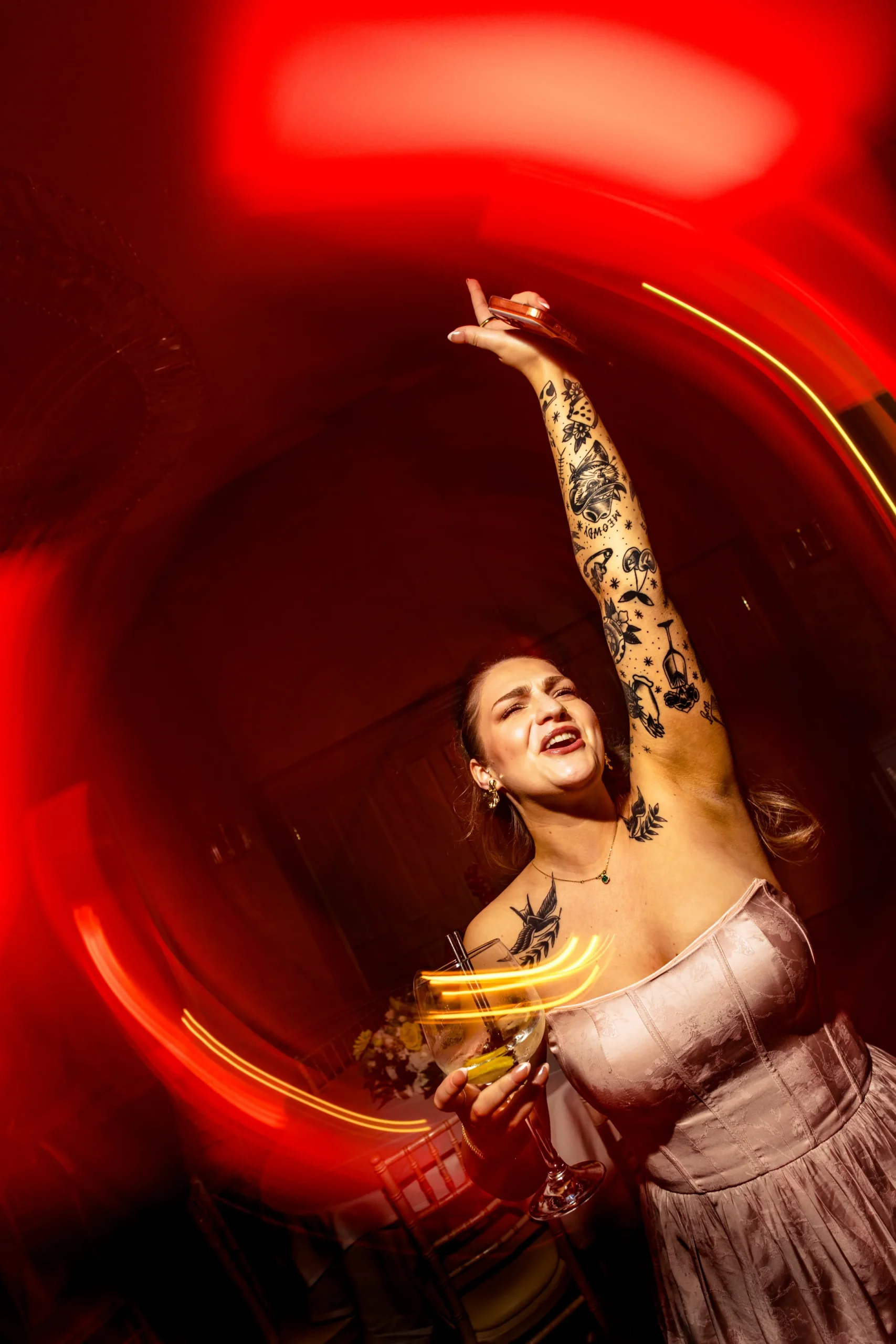A bride raising her arm on the dance floor surrounded by a swirl of red light at Rowton Hall