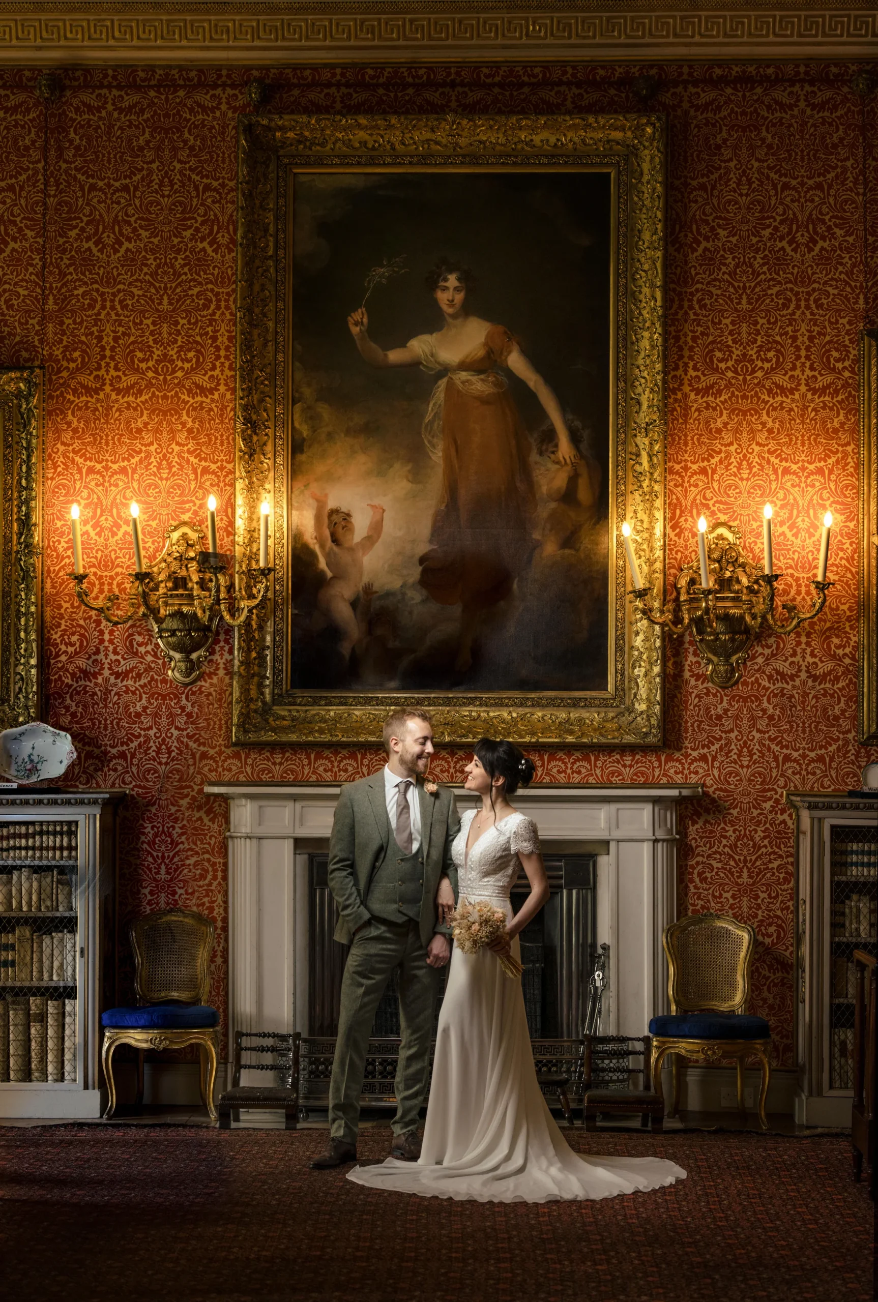 A couple standing beneath a large painting and ornate wall lights at Tabley House