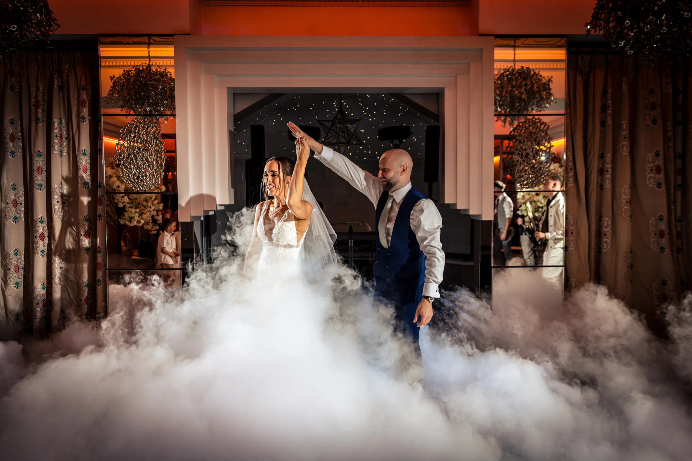 Bride and groom dancing through low mist beneath warm indoor lights