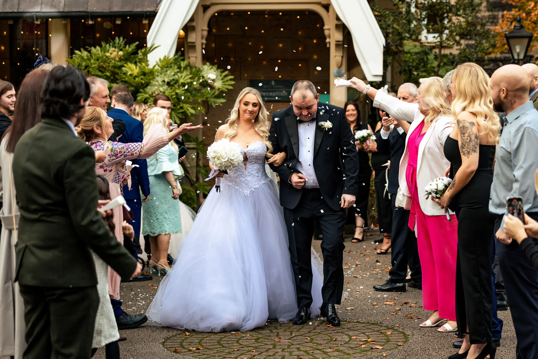 Newlyweds walking through confetti outside a venue, with guests on both sides