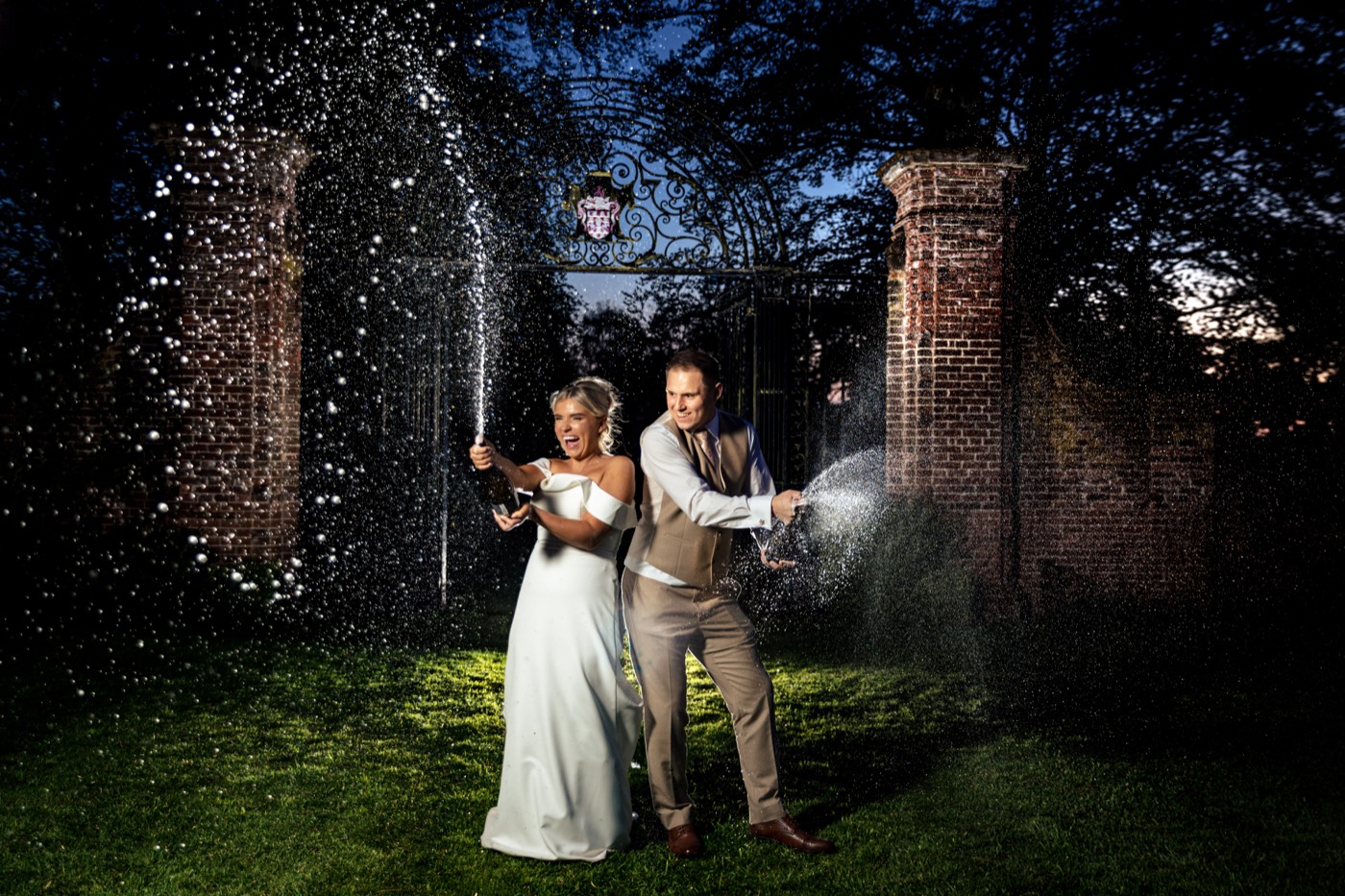 Bride and groom spraying champagne together outside Inglewood Manor at dusk
